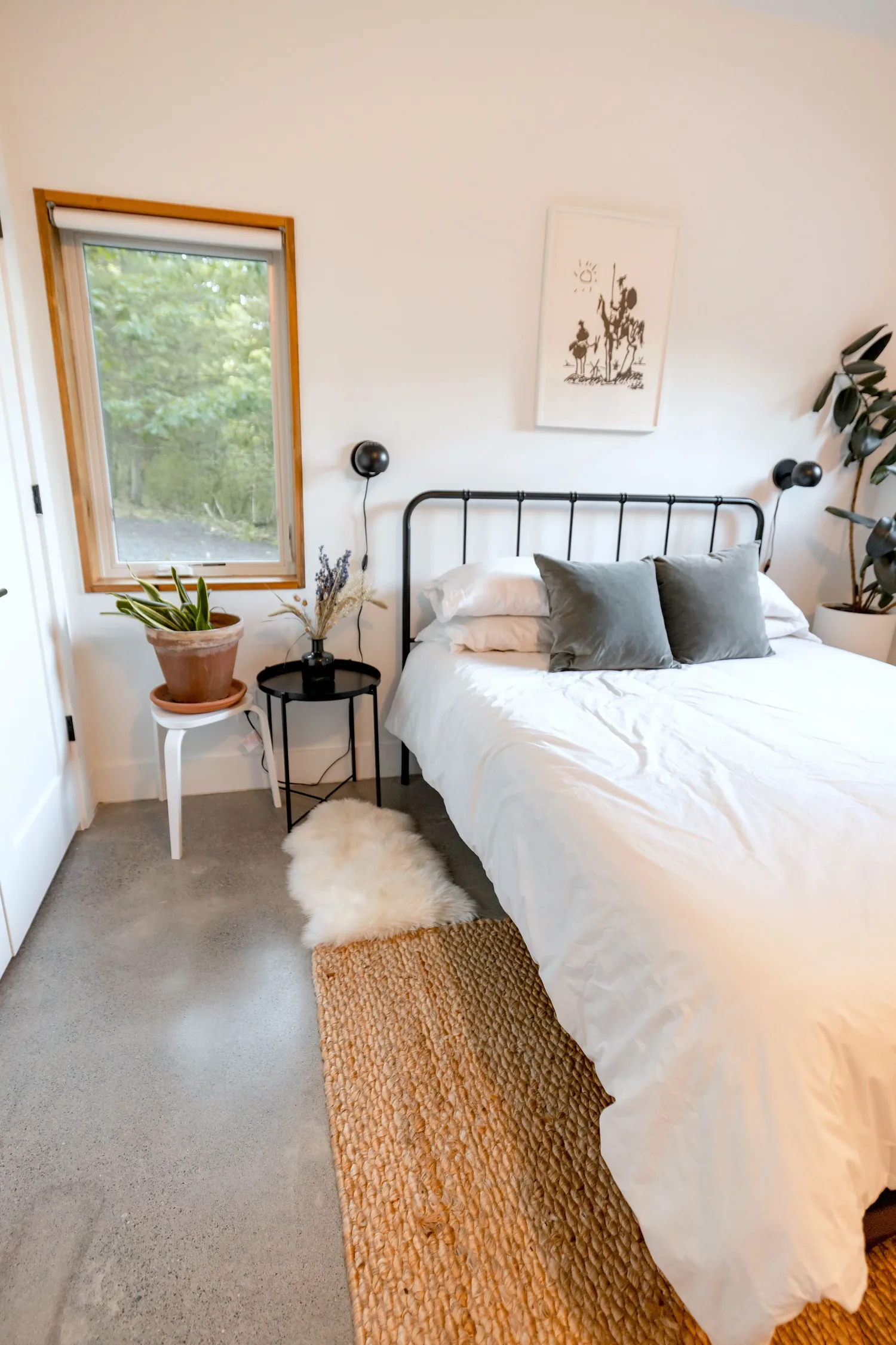 Recámara de Airbnb con cama tendida en blanco, cabecera de herrería y tapete de fibra natural